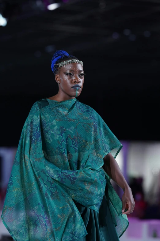 a model wearing a green outfit walking on a runway