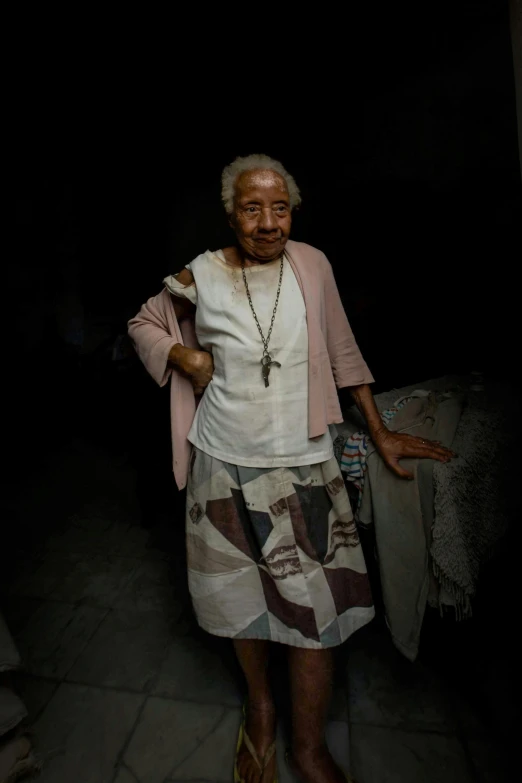 an elderly woman standing by the wall in a darkened area