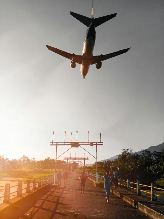 people walking down the walkway under an airplane that is flying