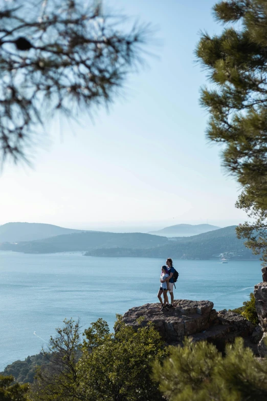 a couple of people standing on top of a mountain near the ocean