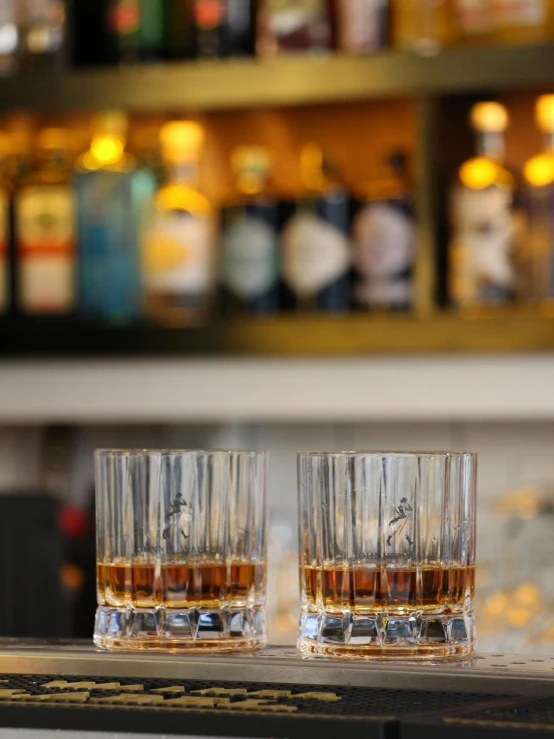 two glasses of whisky on a bar next to bottles