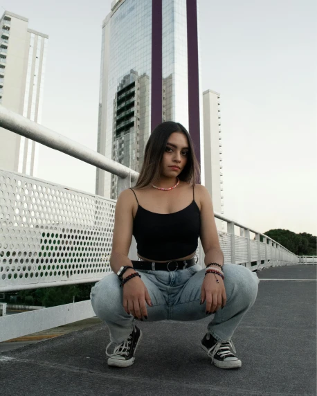 a girl in jeans and a black tank top posing on a bridge