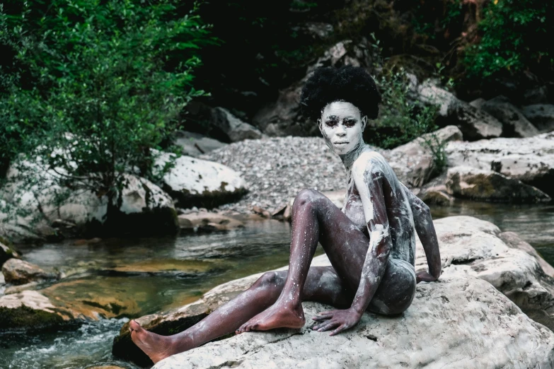 a  woman sitting on a rock by a stream