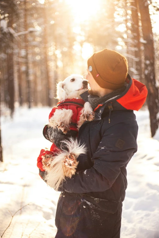 man holding dog in winter clothes while standing outside