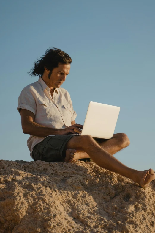 there is a man that is sitting on a rock with a laptop