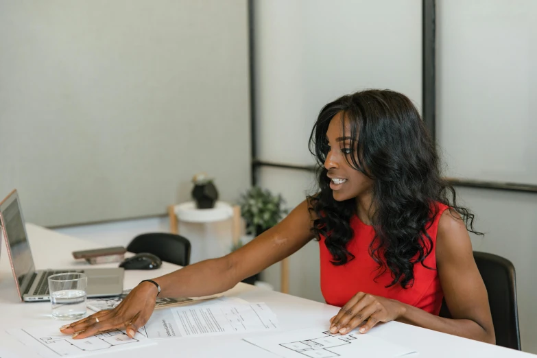 a woman wearing a red dress is smiling as she signs paperwork in front of her