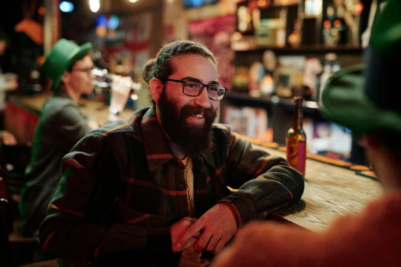 a bearded man is smiling at the camera with another person in the backgrond