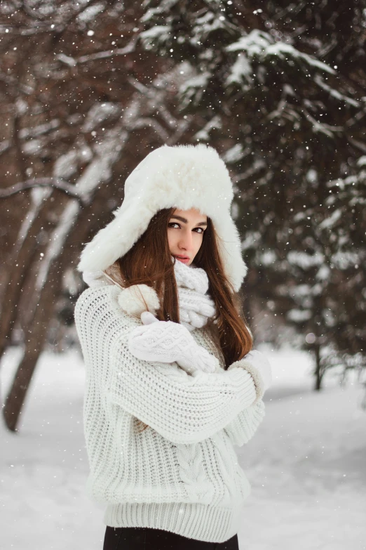 a woman stands in the snow and wearing a white hat and sweater