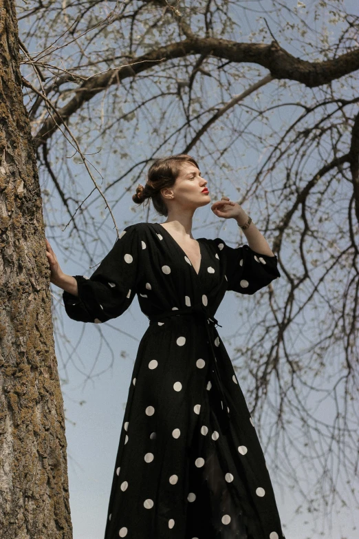 a woman wearing a polka dot dress is posing by a tree