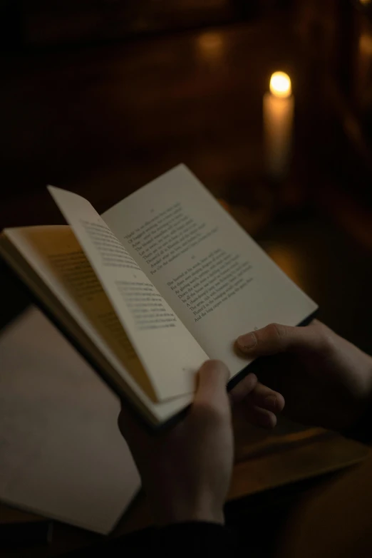 a hand holding an open book with candle light on the side