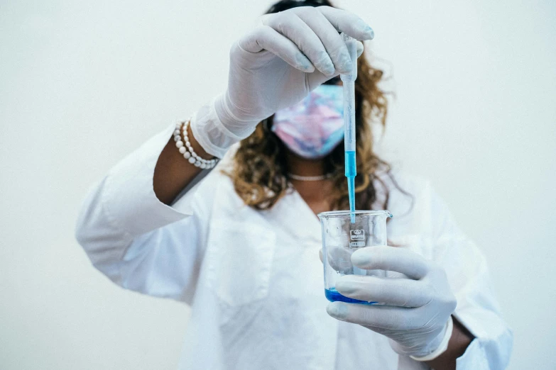 a person holding a glass and tubes wearing a white lab coat