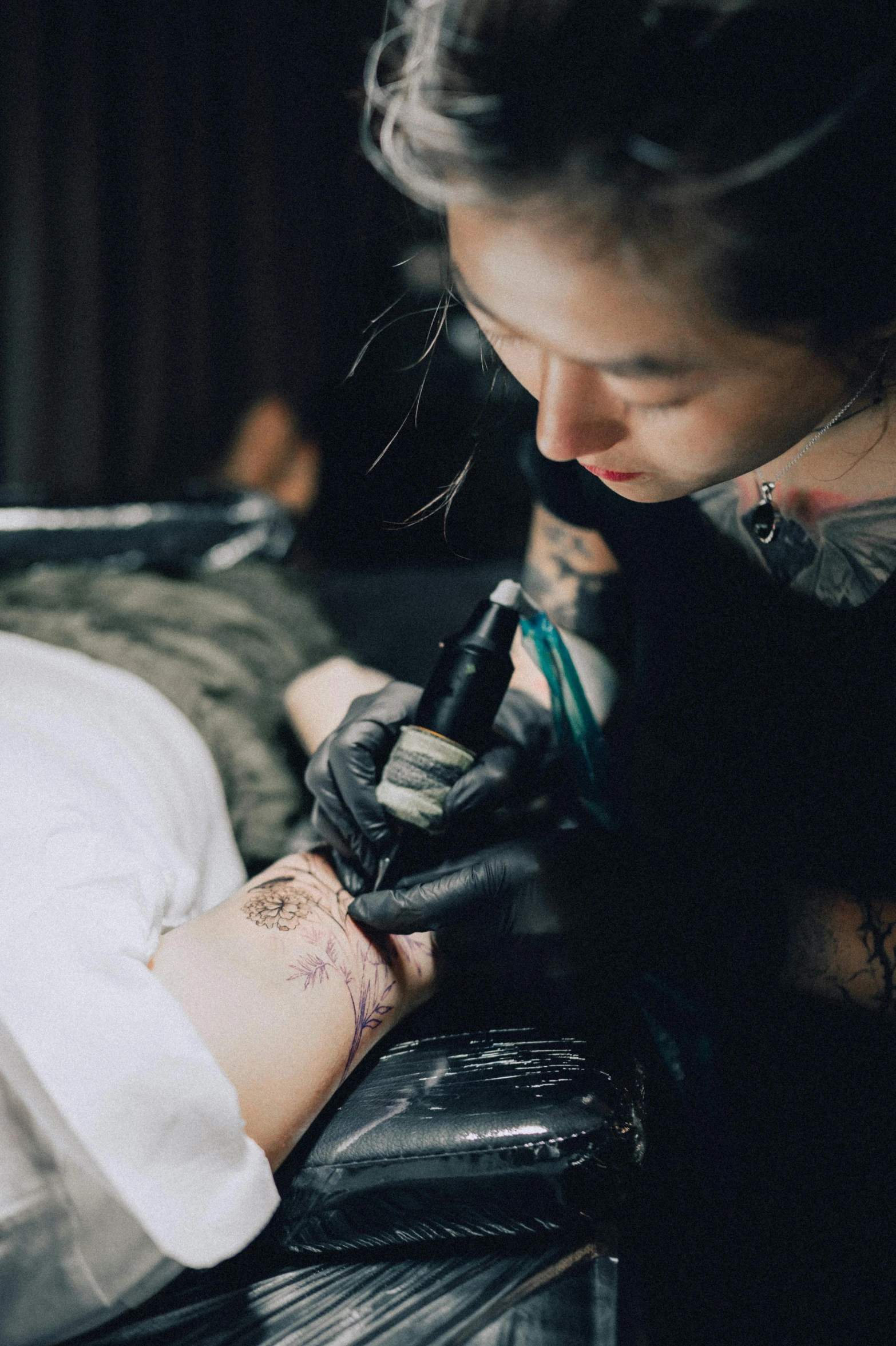 woman getting tattoo done on arm in dark room