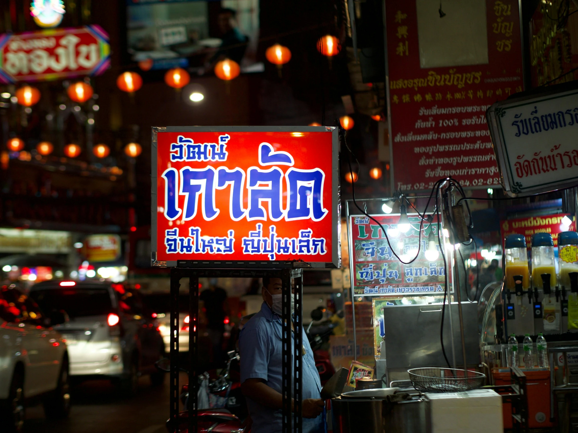 a man walking down a street past stores with neon signs