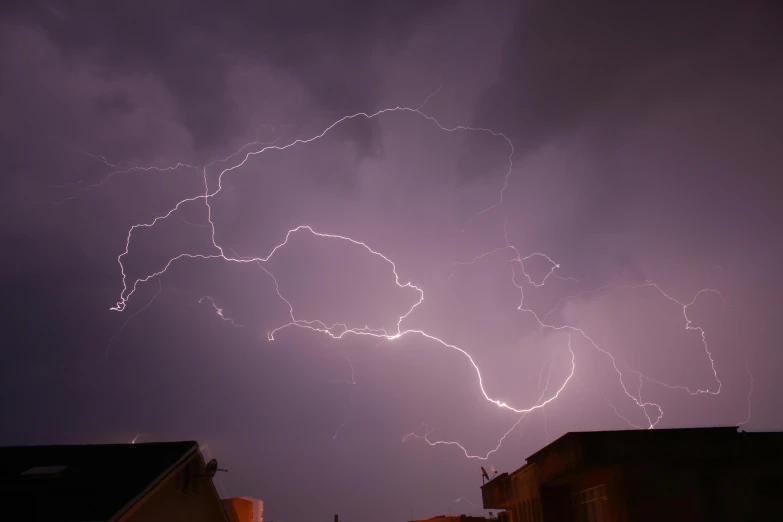 a purple sky with lightening and thunder behind buildings