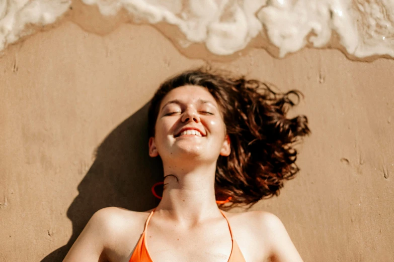 a woman wearing a orange bikini lying on the beach