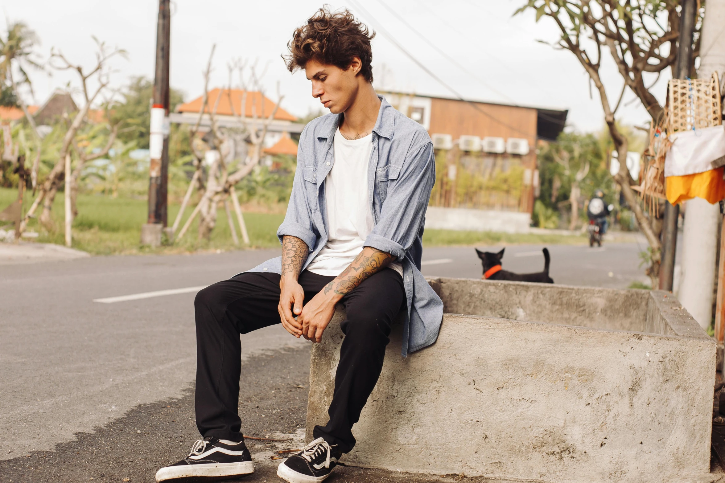 a young man with tattooed arm sitting on concrete