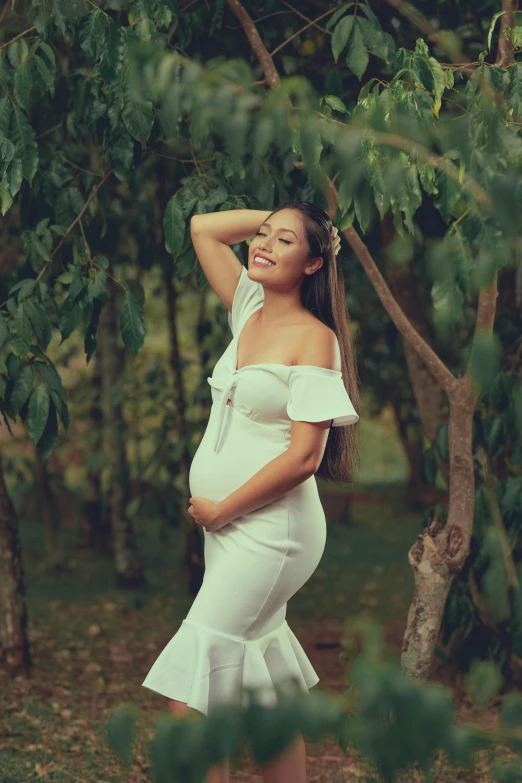 a pregnant woman in white dress poses for a po