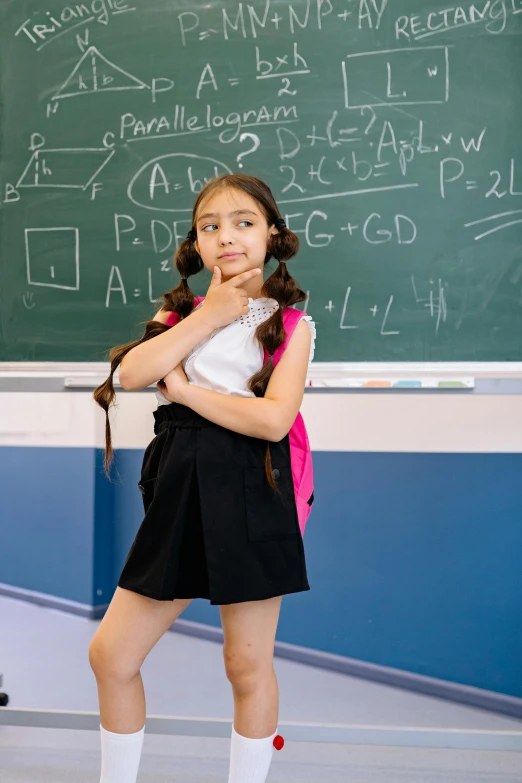 a young female wearing a skirt and white socks in front of a blackboard