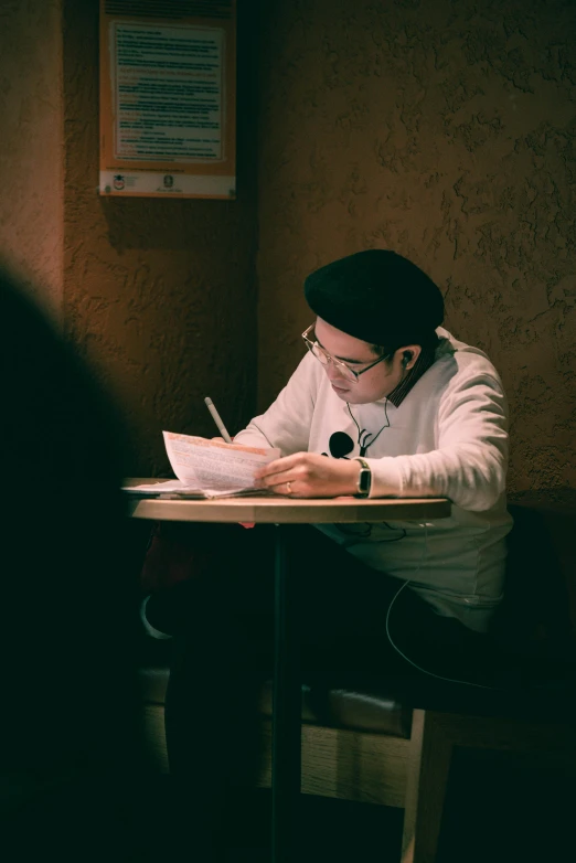 a young woman sitting at a table in a corner writing