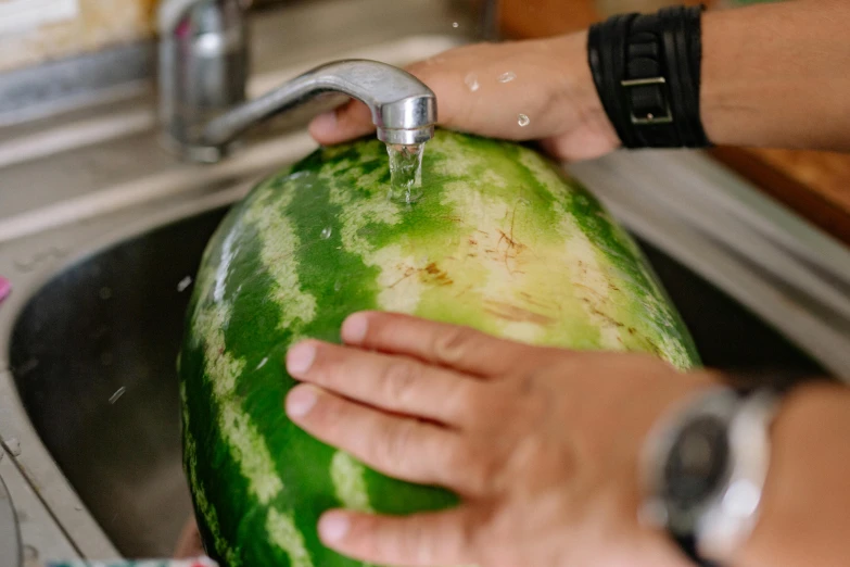 a watermelon being washed by someone at the sink