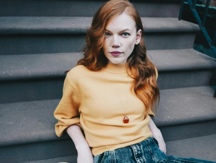 a woman sitting on some steps wearing a yellow sweater