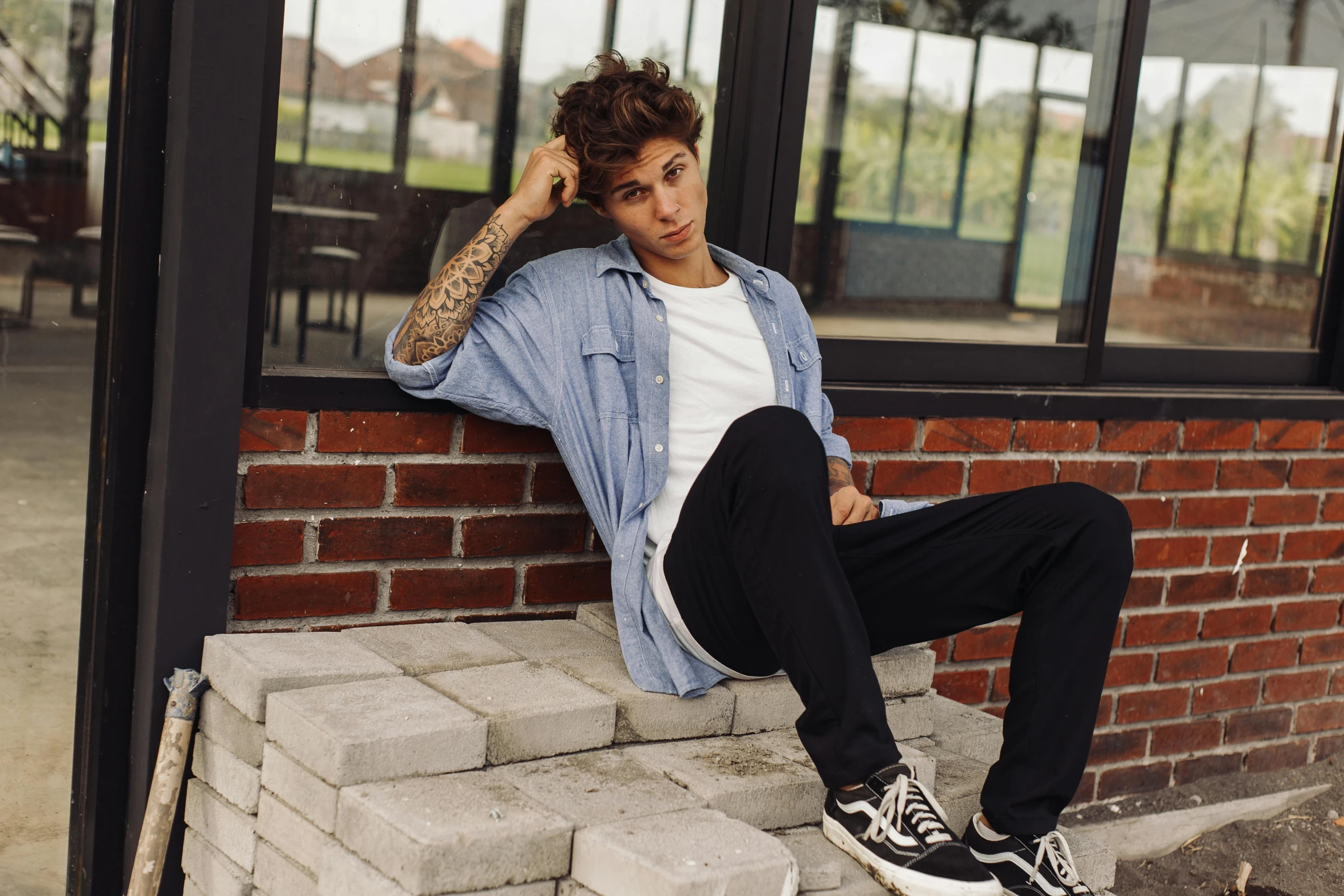 a man sits against a brick wall while smoking a cigarette