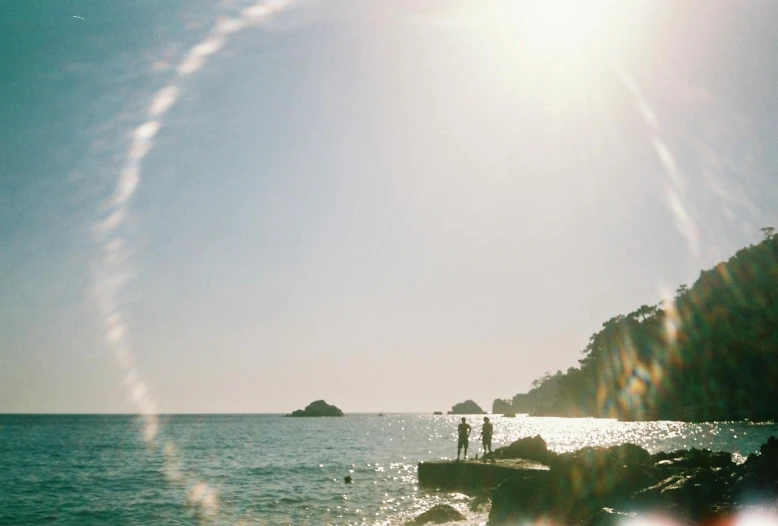 two people standing on a rocky shore at the beach