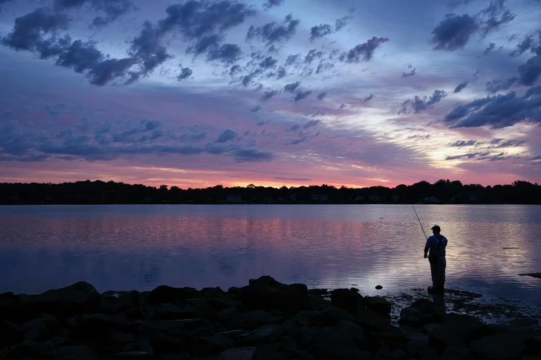 a lone fisherman fishing off the coast as the sun rises