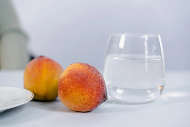 the two peaches are next to the glass of water