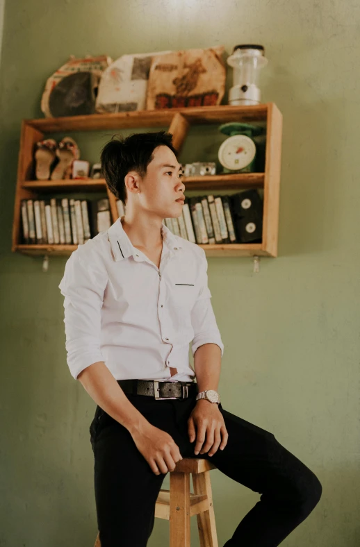 a man sitting on top of a stool near a wooden shelf