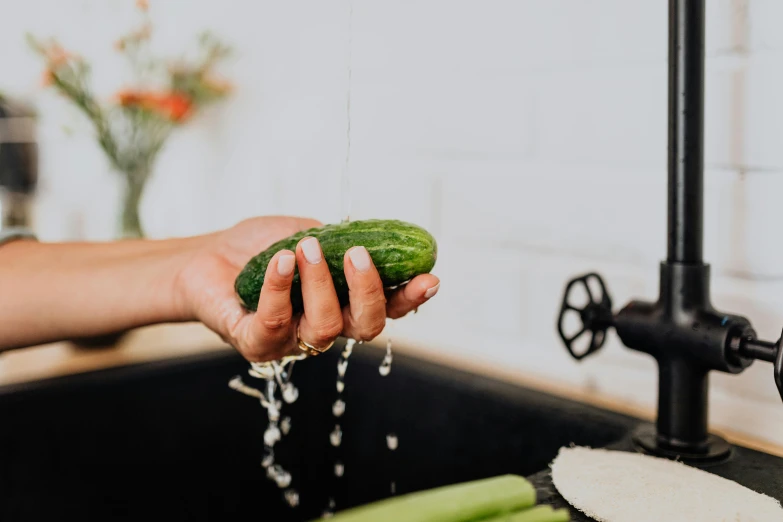 someone washing a cucumber over a sink