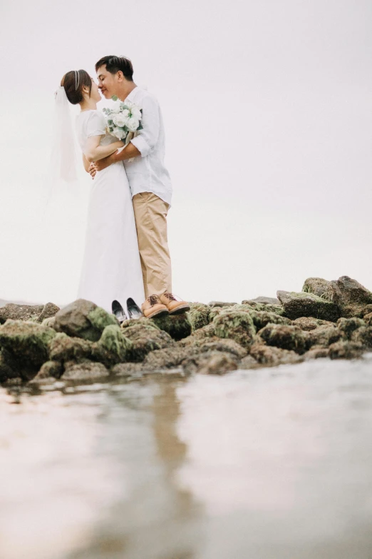 a man and woman hugging on the rocks by water