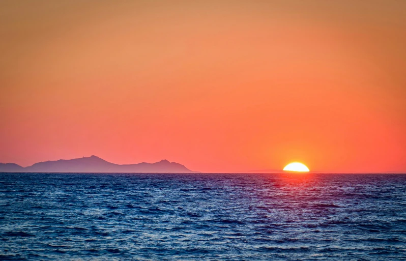 the setting sun over mountains on the ocean