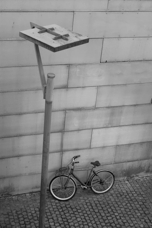 a bicycle  to a pole next to a wall