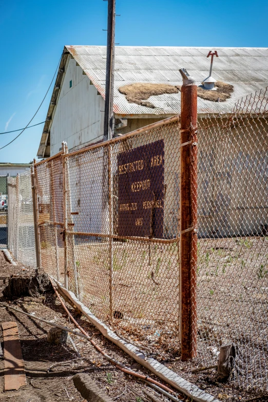 the rusted old train yard fence has rust on it and a sign on the wood post