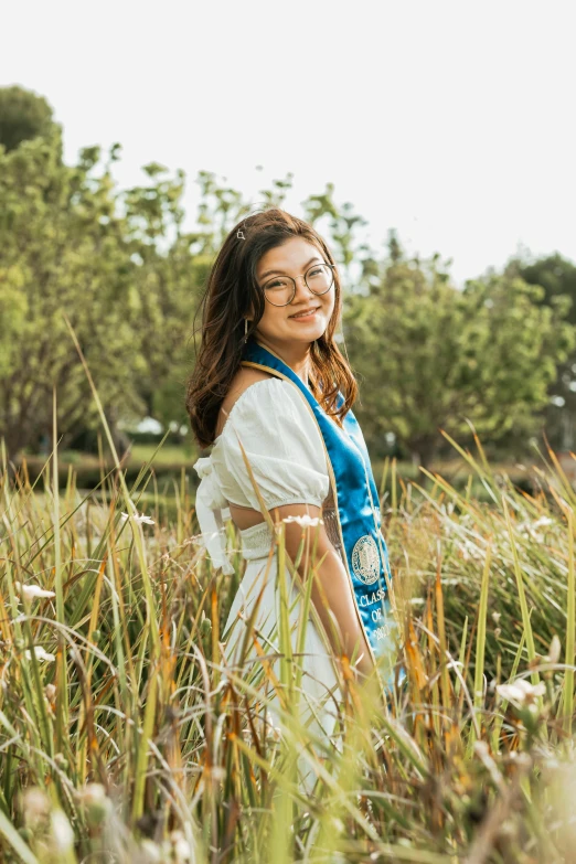 an asian woman standing in tall grass wearing a blue ribbon