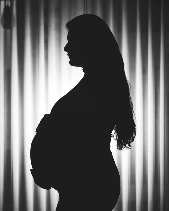 a pregnant woman's stomach and silhouette in front of a curtain