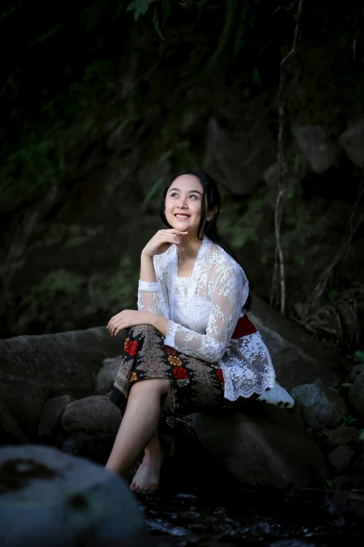 a woman is sitting on rocks and posing for the camera