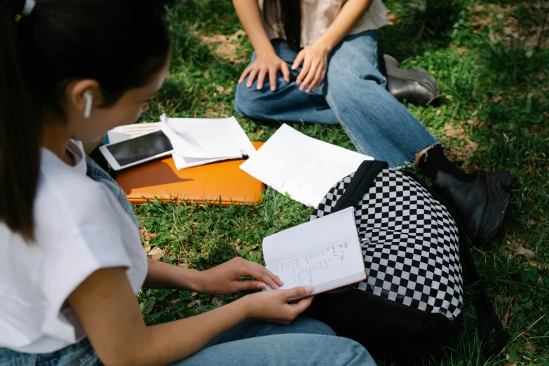 two girls sit in the grass and hold notebooks