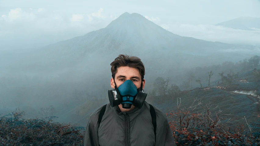 man wearing a gas mask and jacket near top of mountain