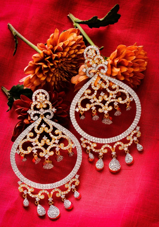 pair of white and yellow gold earrings on a red cloth with flowers