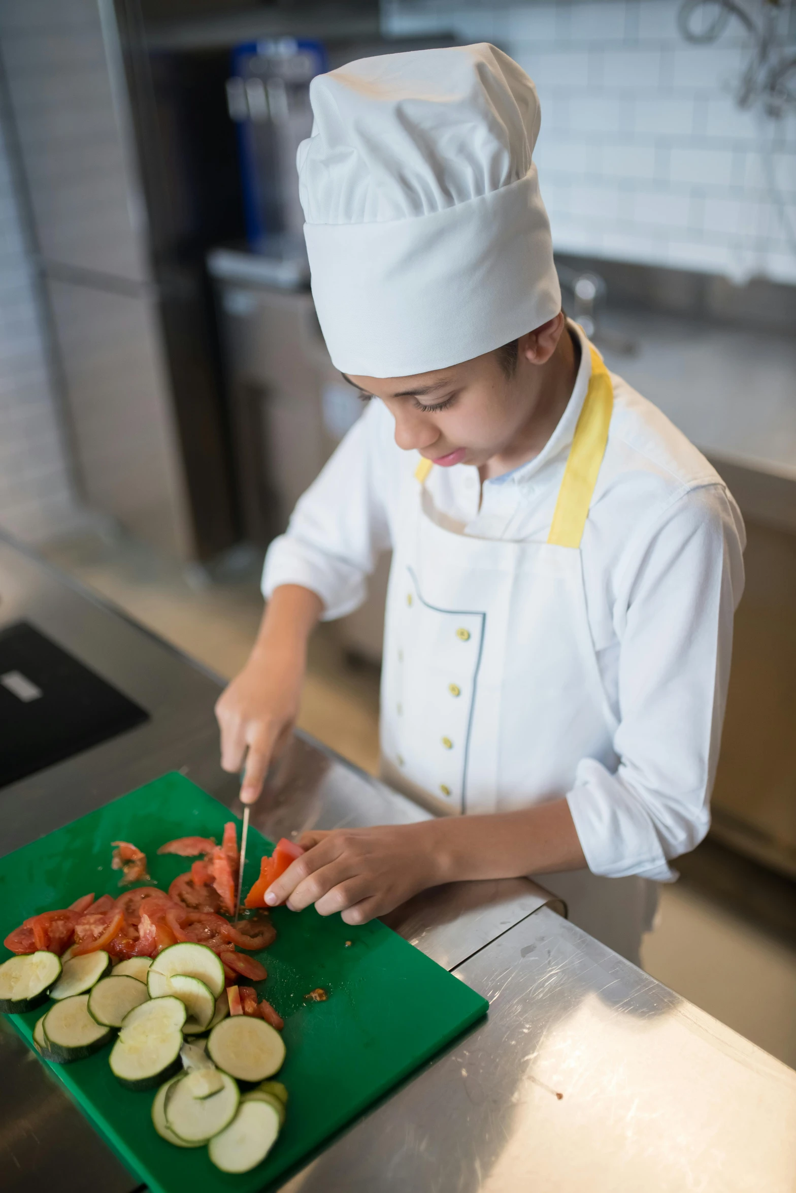 a boy in a chef's uniform chopping up a vegetable