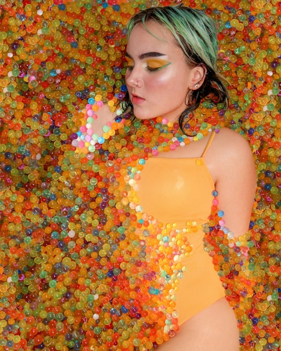 a girl is wearing yellow and is surrounded by a pile of small candy