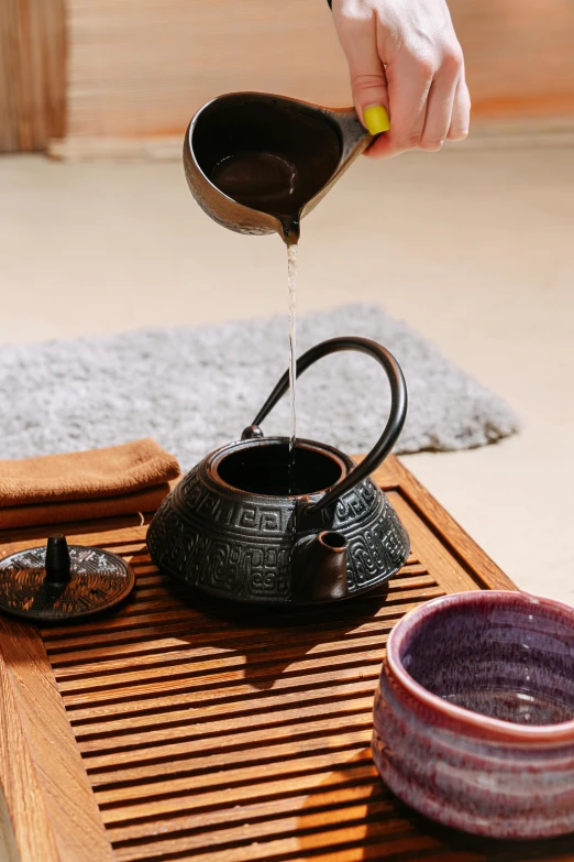 person pouring coffee into a black teapot on top of a wooden mat