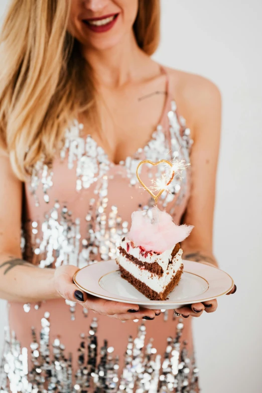 a woman wearing a sequins dress is holding a slice of cake