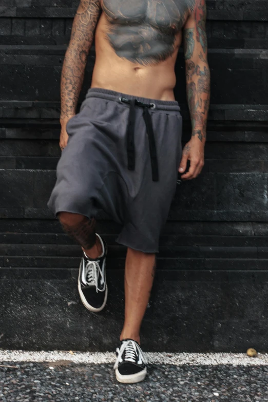 a man in shorts with tattoos is sitting against a wall