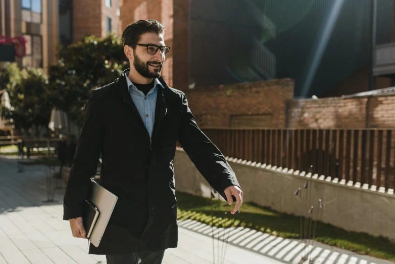 a bearded man walking in the city with his notebook