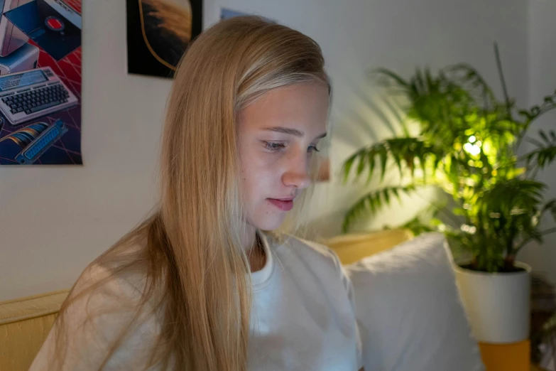 a blonde girl with long hair and a white blouse sitting on a bed with a laptop