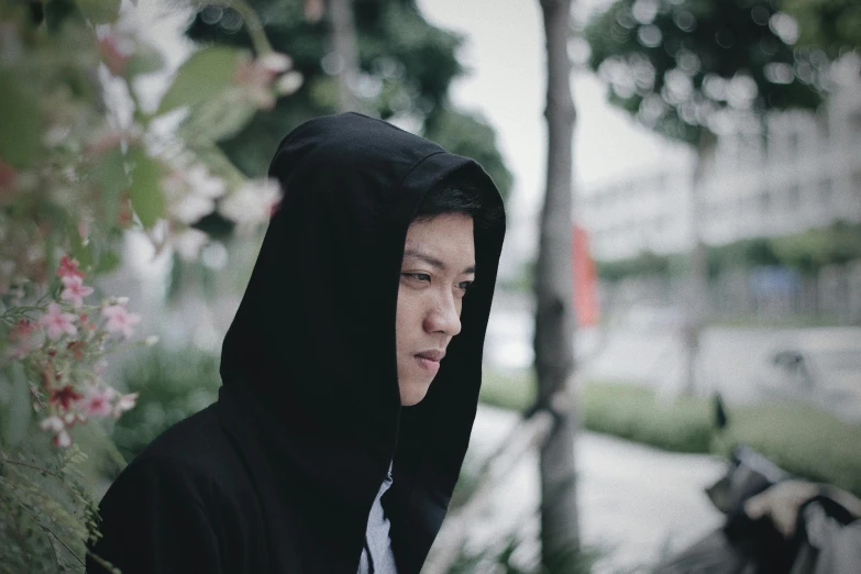 a man in hoodie standing by a plant with flowers