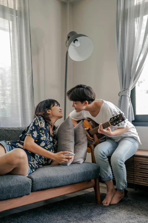 a woman sits on a couch while a man plays the guitar